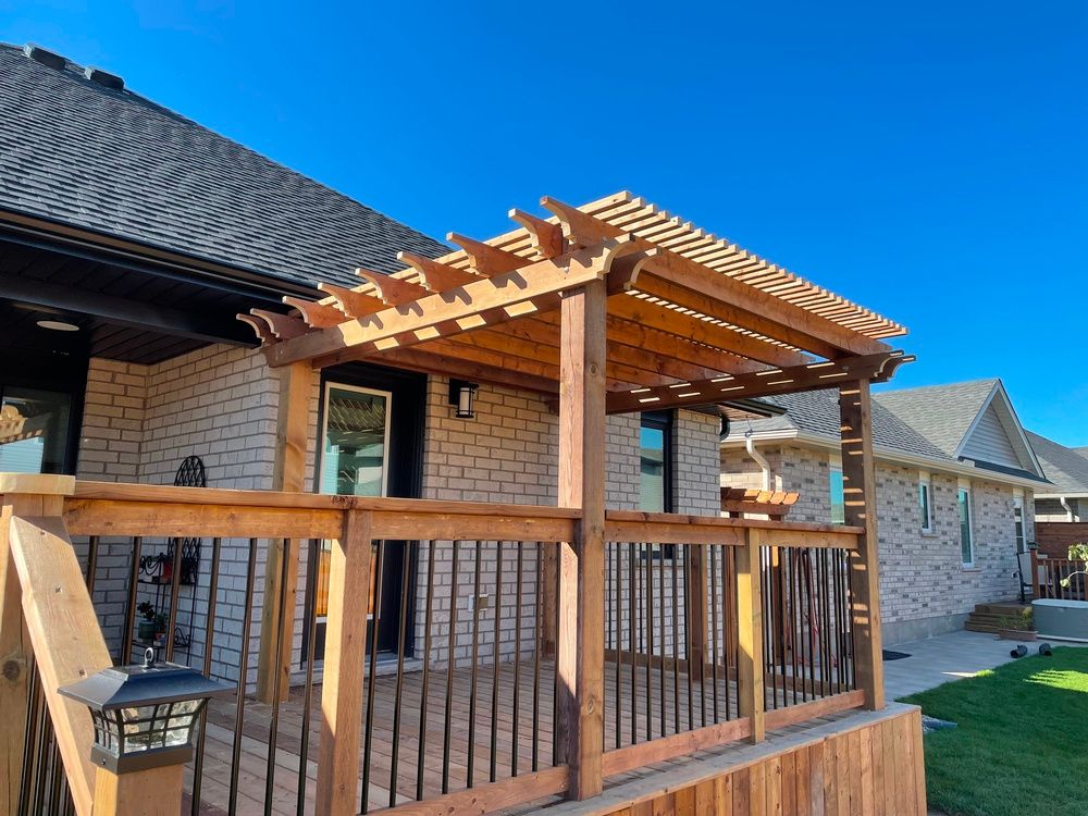 A wooden deck with a pergola on top of it in front of a brick house.