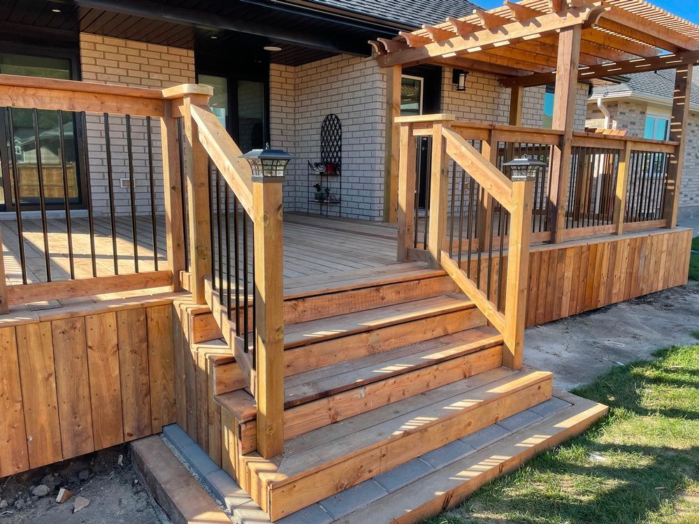 A wooden deck with stairs and a pergola in front of a brick house.