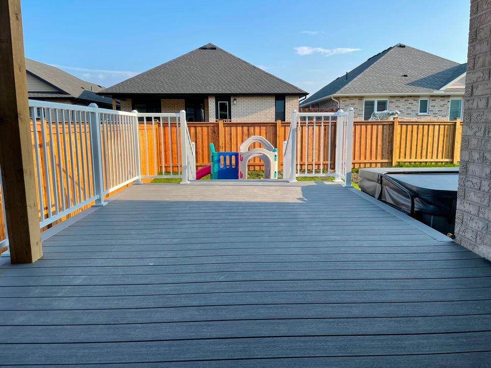 A deck with a fence and a playground in the backyard of a house.