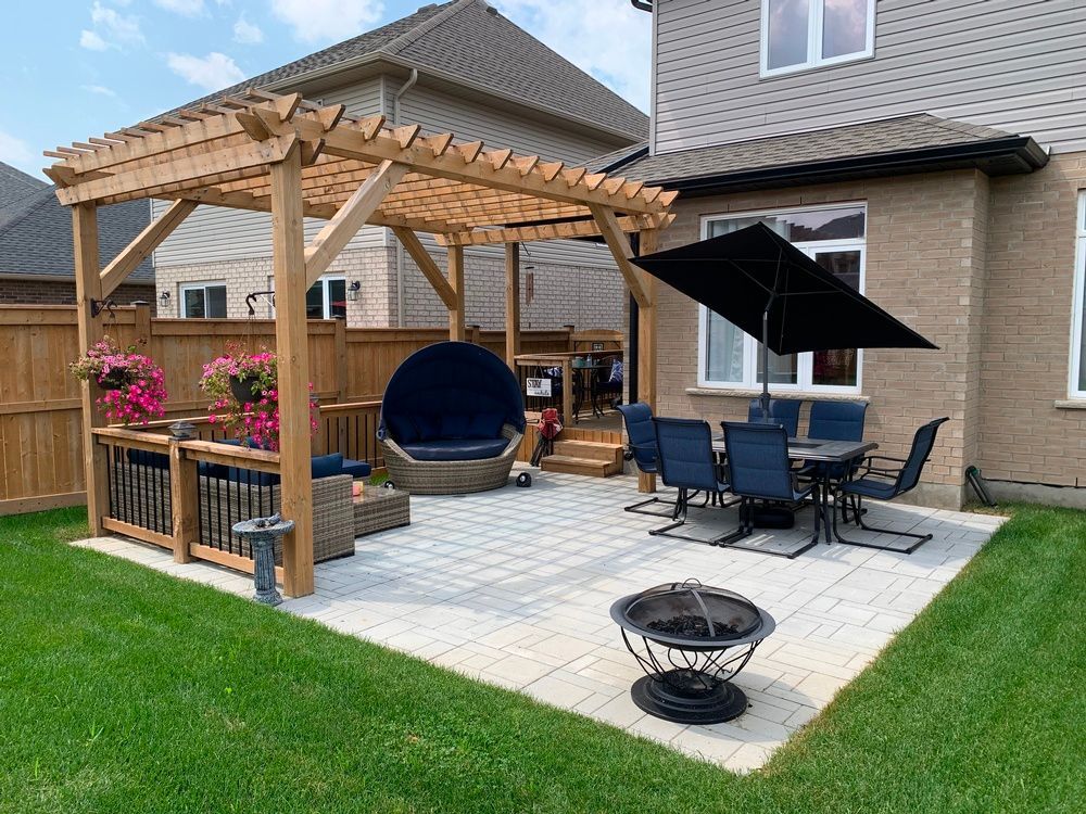 A backyard with a pergola , table and chairs and a fire pit.