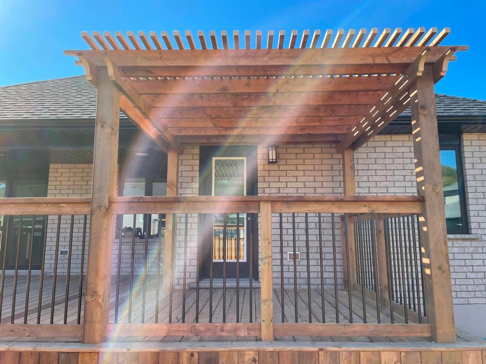 A wooden deck with a pergola on top of it in front of a brick house.