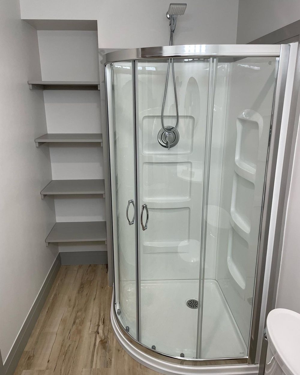 A bathroom with a shower , toilet and shelves.