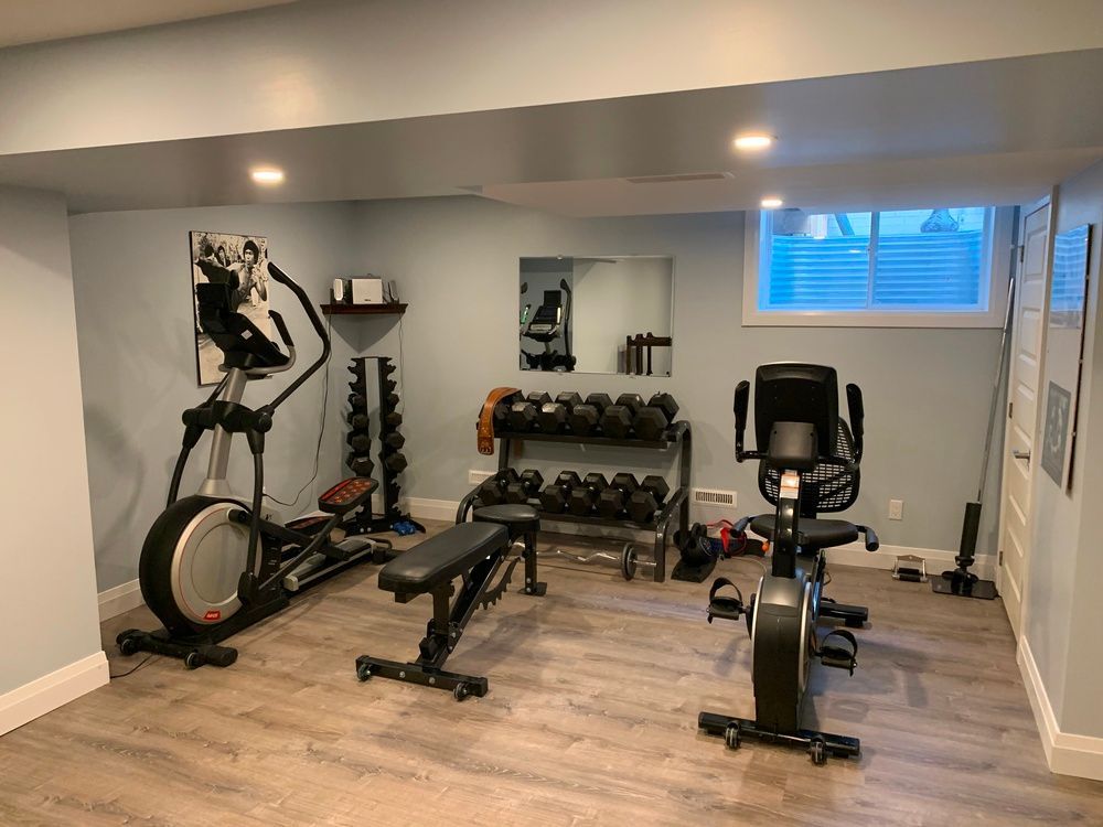 A basement gym with exercise bikes , dumbbells , and a bench.