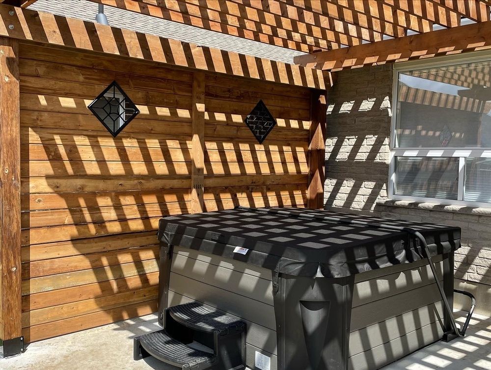 A hot tub is sitting under a wooden pergola.