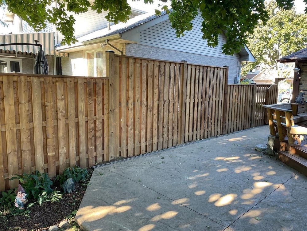 A wooden fence surrounds a concrete walkway in front of a house.