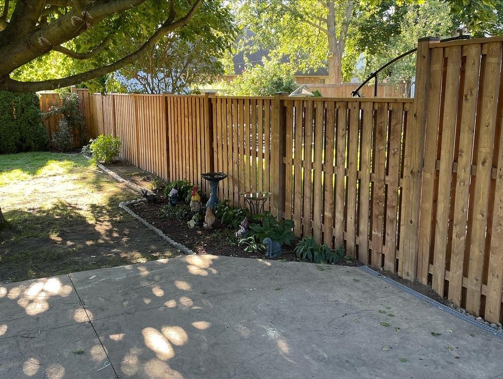 A wooden fence surrounds a concrete driveway in a backyard.
