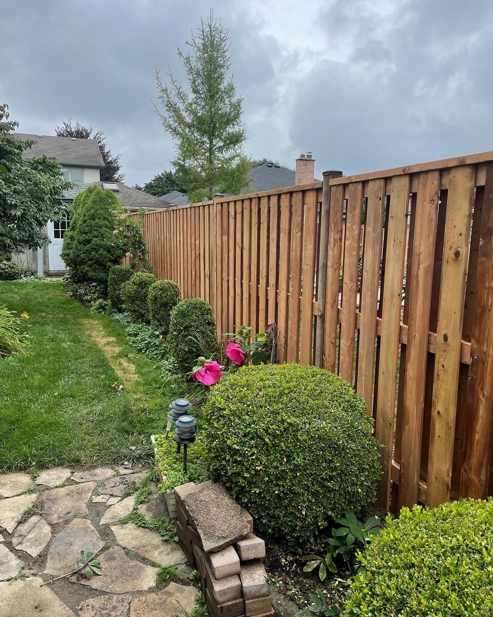 A wooden fence is surrounded by flowers and bushes in a backyard.
