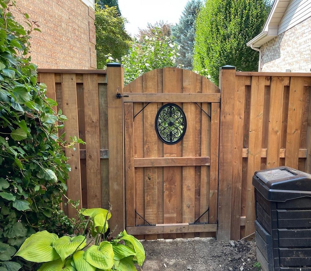 A wooden gate with a clock on it is surrounded by a wooden fence.