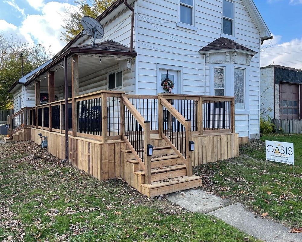 A white house with a wooden deck and stairs in front of it.