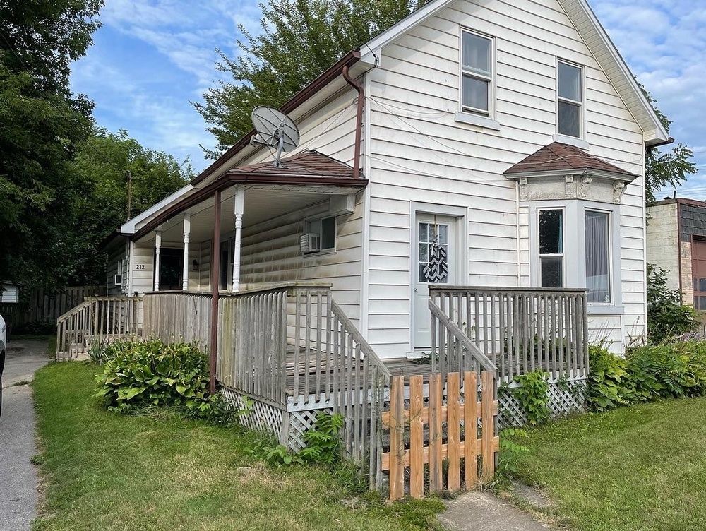 A white house with a porch and a satellite dish on the roof.