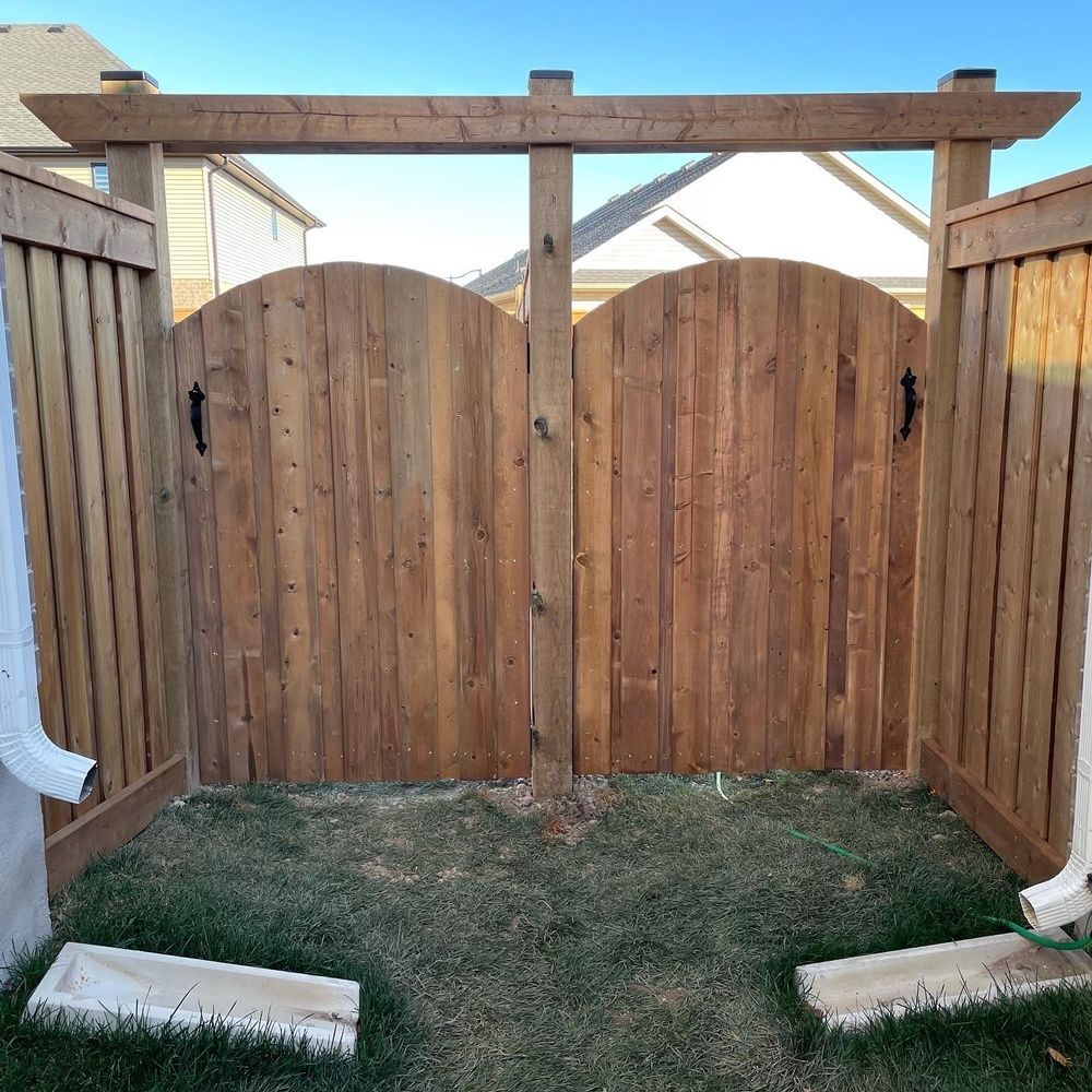 A wooden fence with a gate and a pergola in the backyard.
