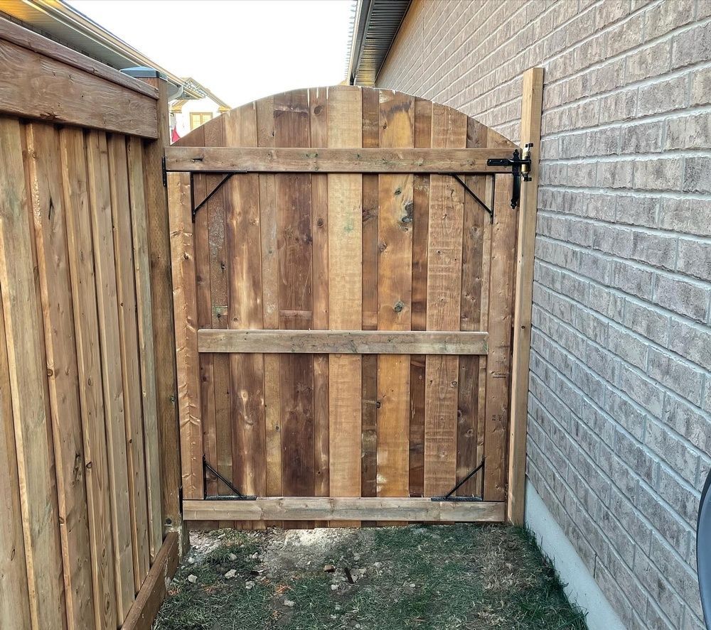 A wooden gate is between a fence and a brick wall.