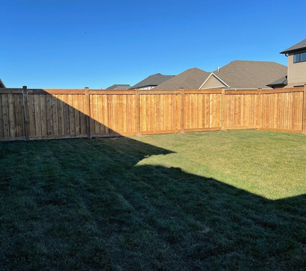 A wooden fence surrounds a lush green lawn in a backyard.