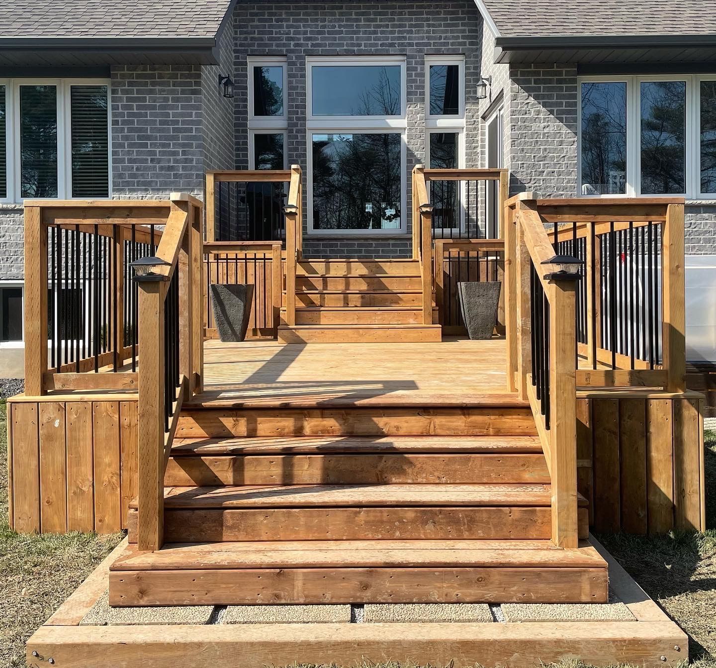 A wooden deck with stairs leading up to it is in front of a brick house.
