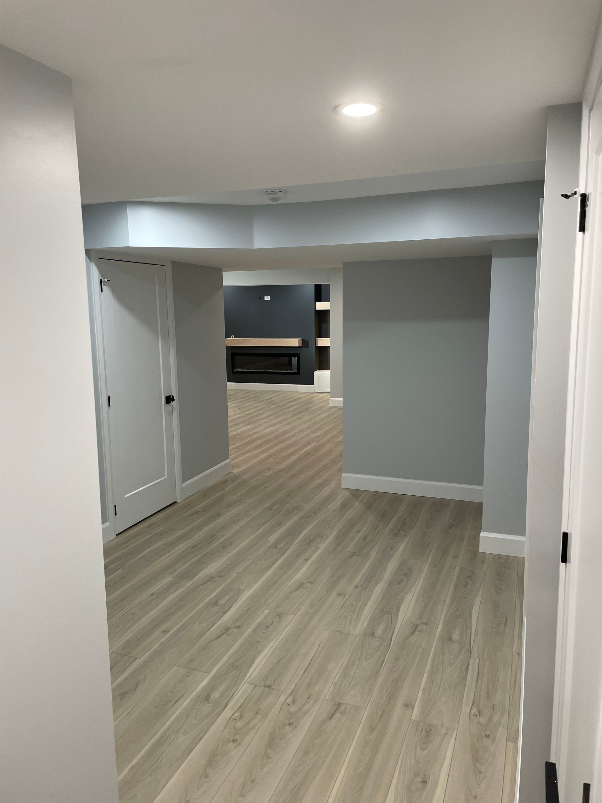 A hallway in a basement with hardwood floors and a fireplace.
