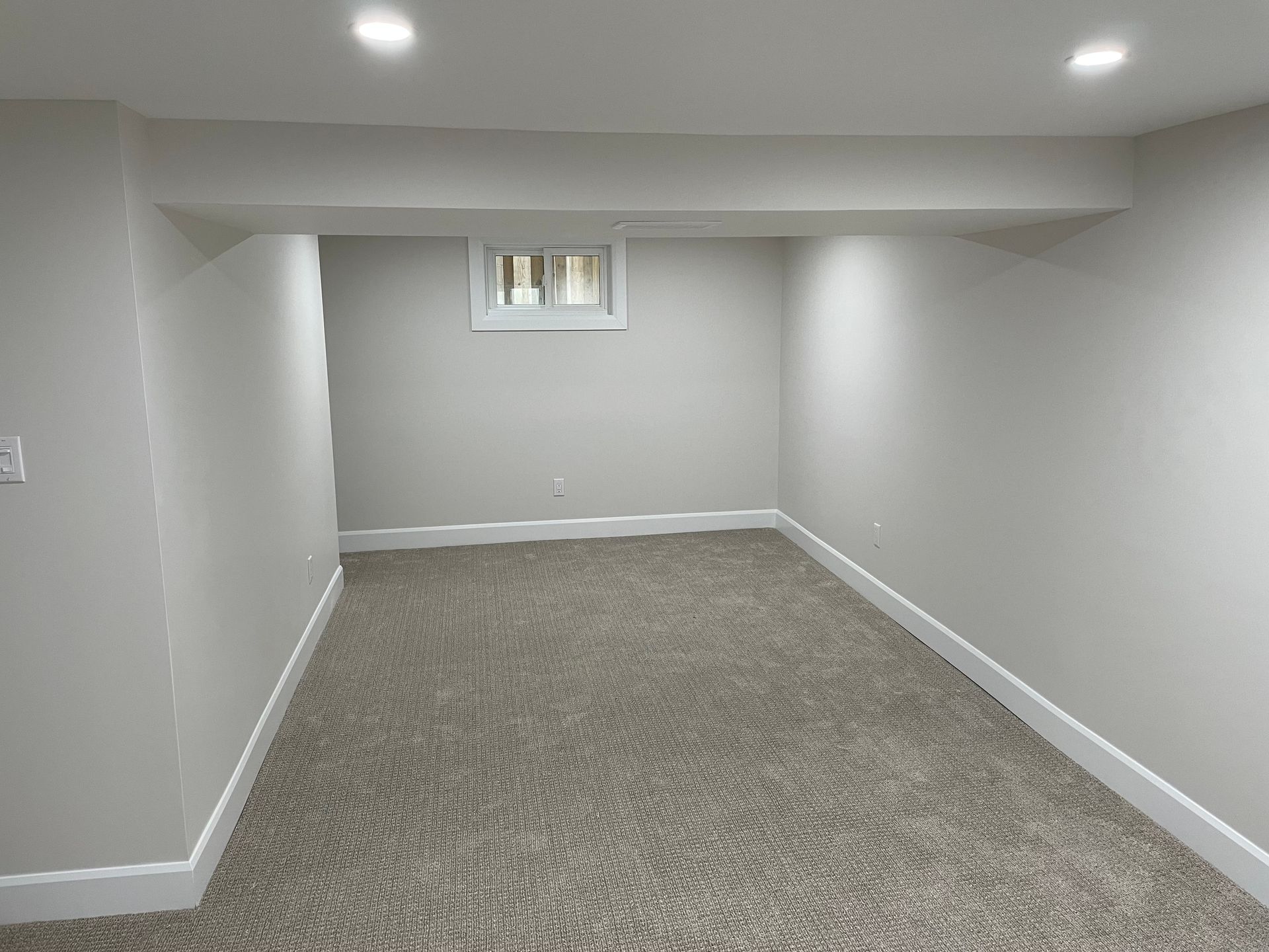 An empty basement with a window and carpet.