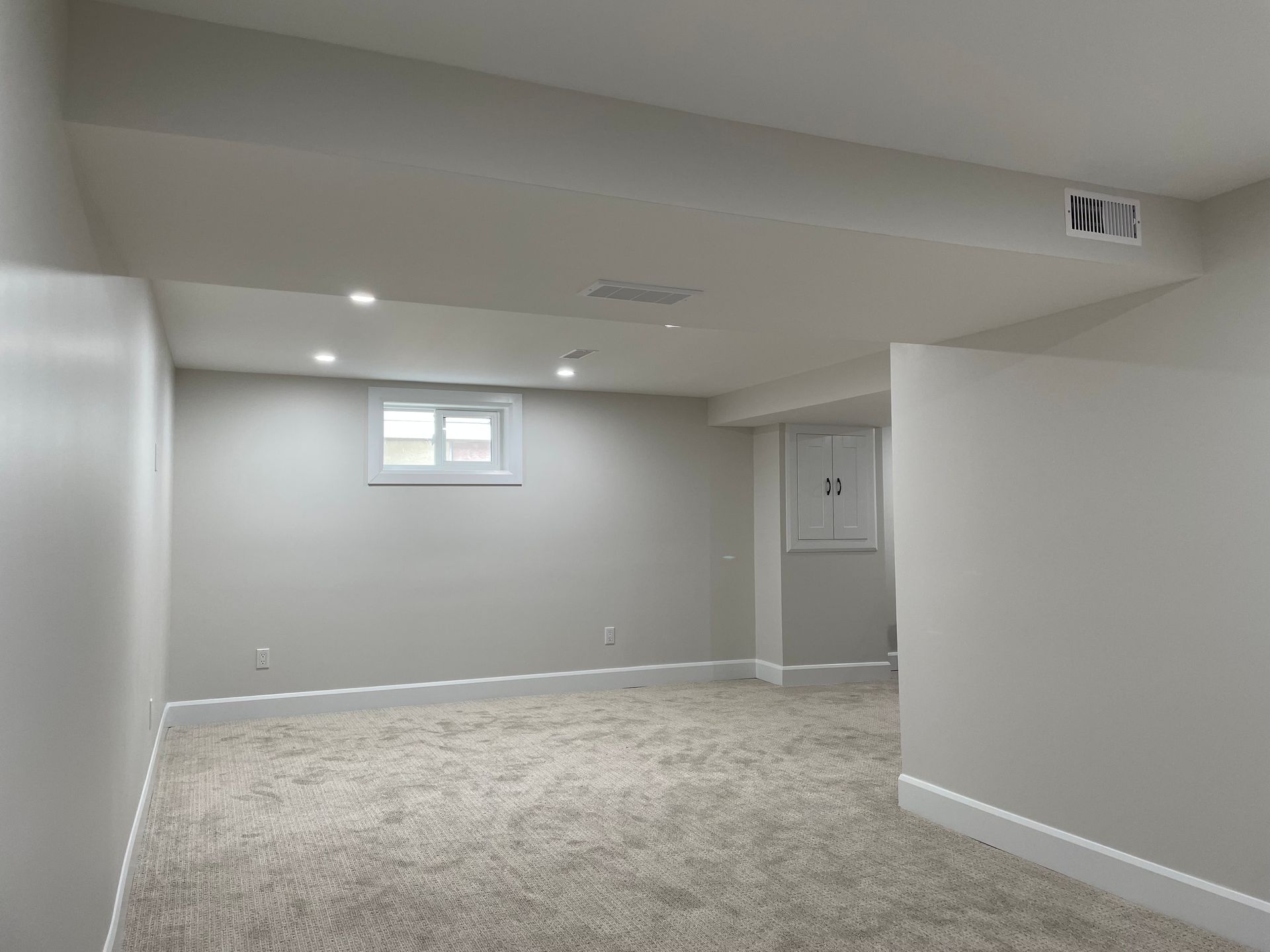 An empty basement with carpeted floors and white walls.