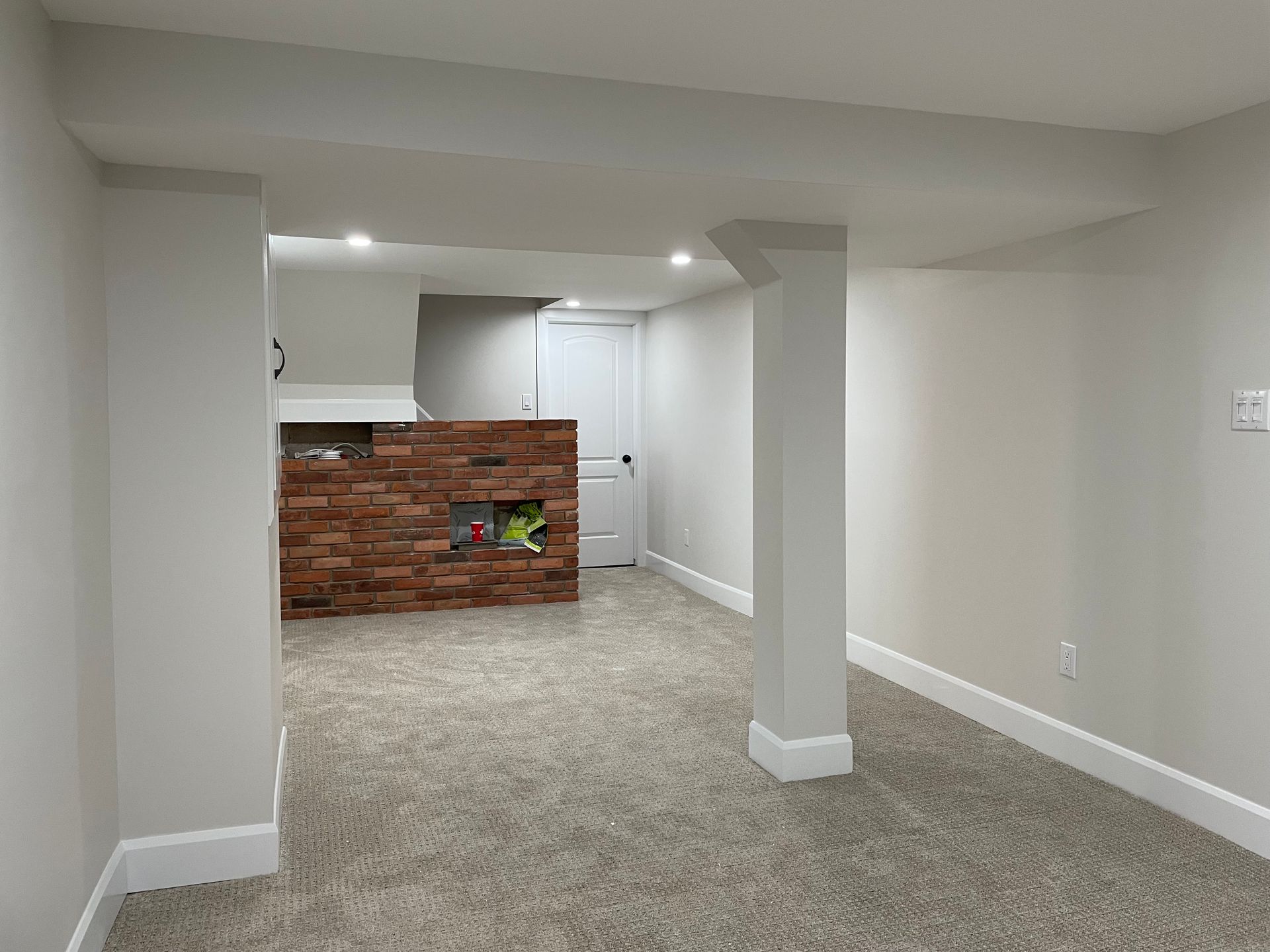 An empty basement with a brick wall and carpeted floor.