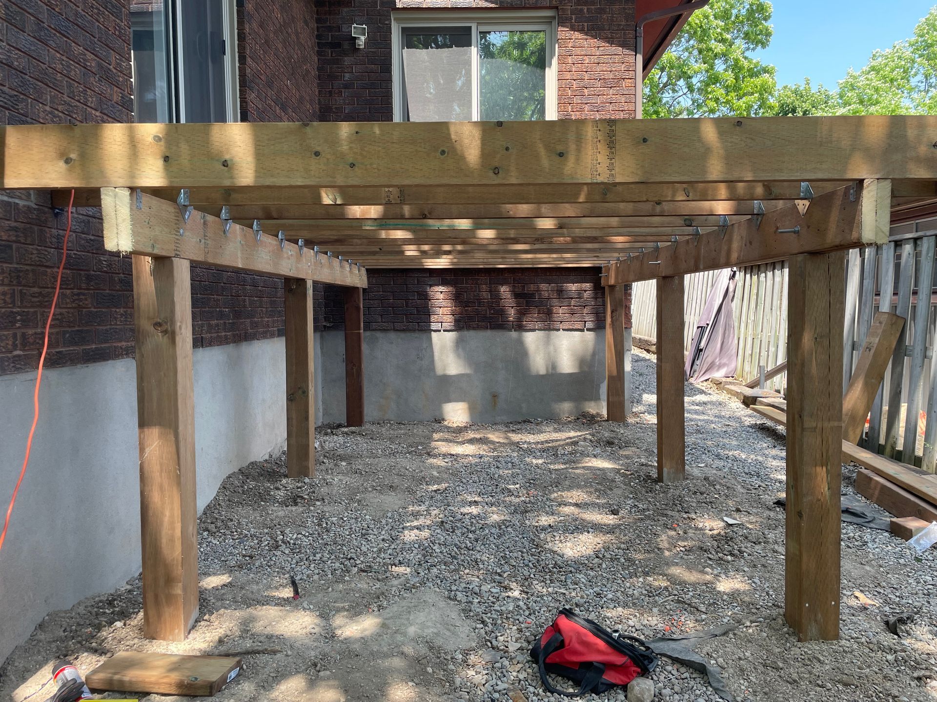 A wooden deck is being built in front of a brick house.