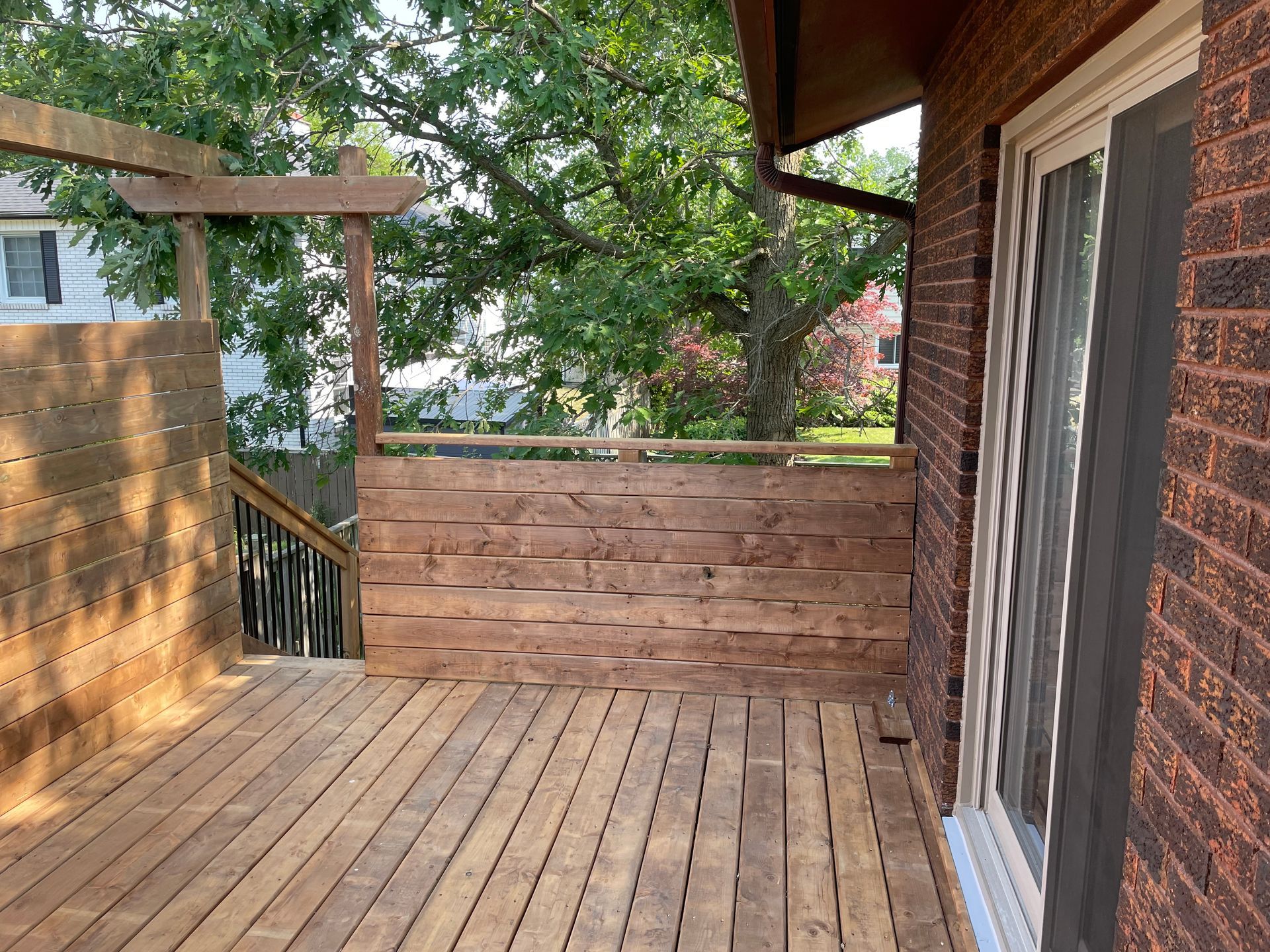 A wooden deck on the side of a brick house with a sliding glass door.