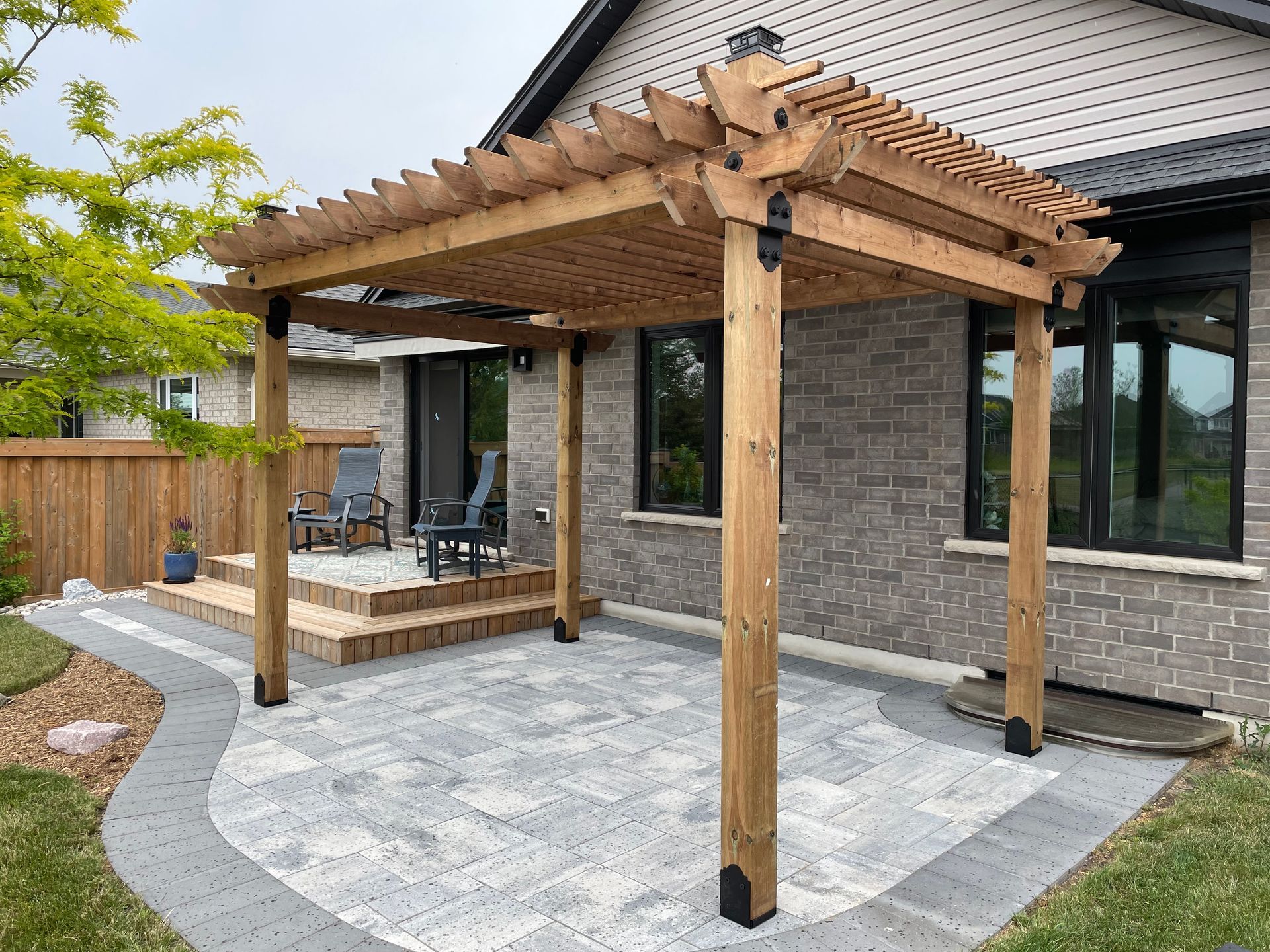 A wooden pergola is sitting on top of a patio in front of a brick house.