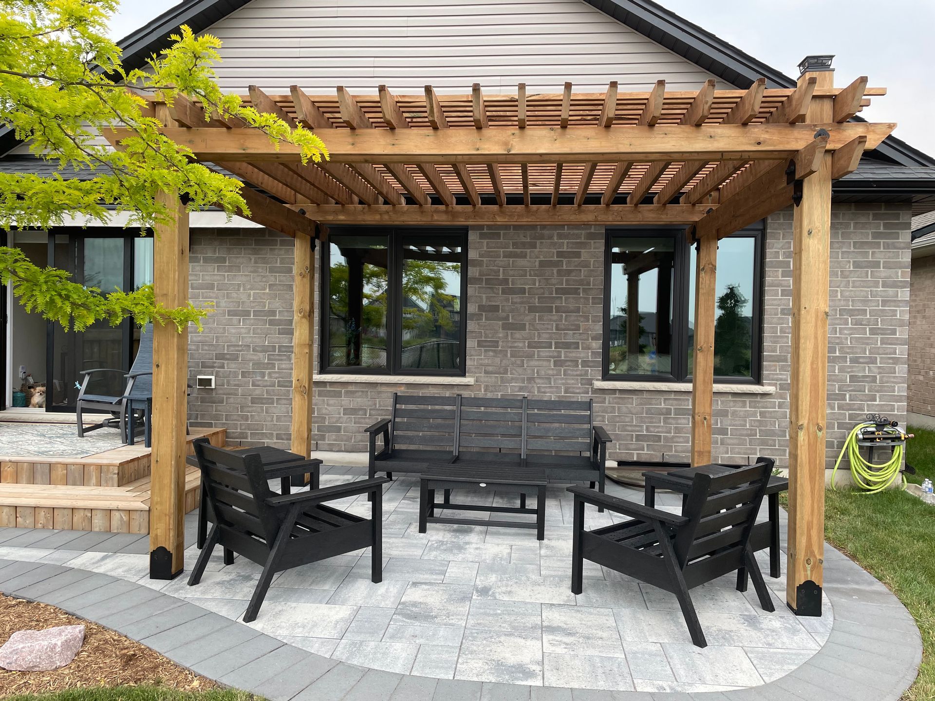 A patio with a pergola and chairs in front of a brick house.
