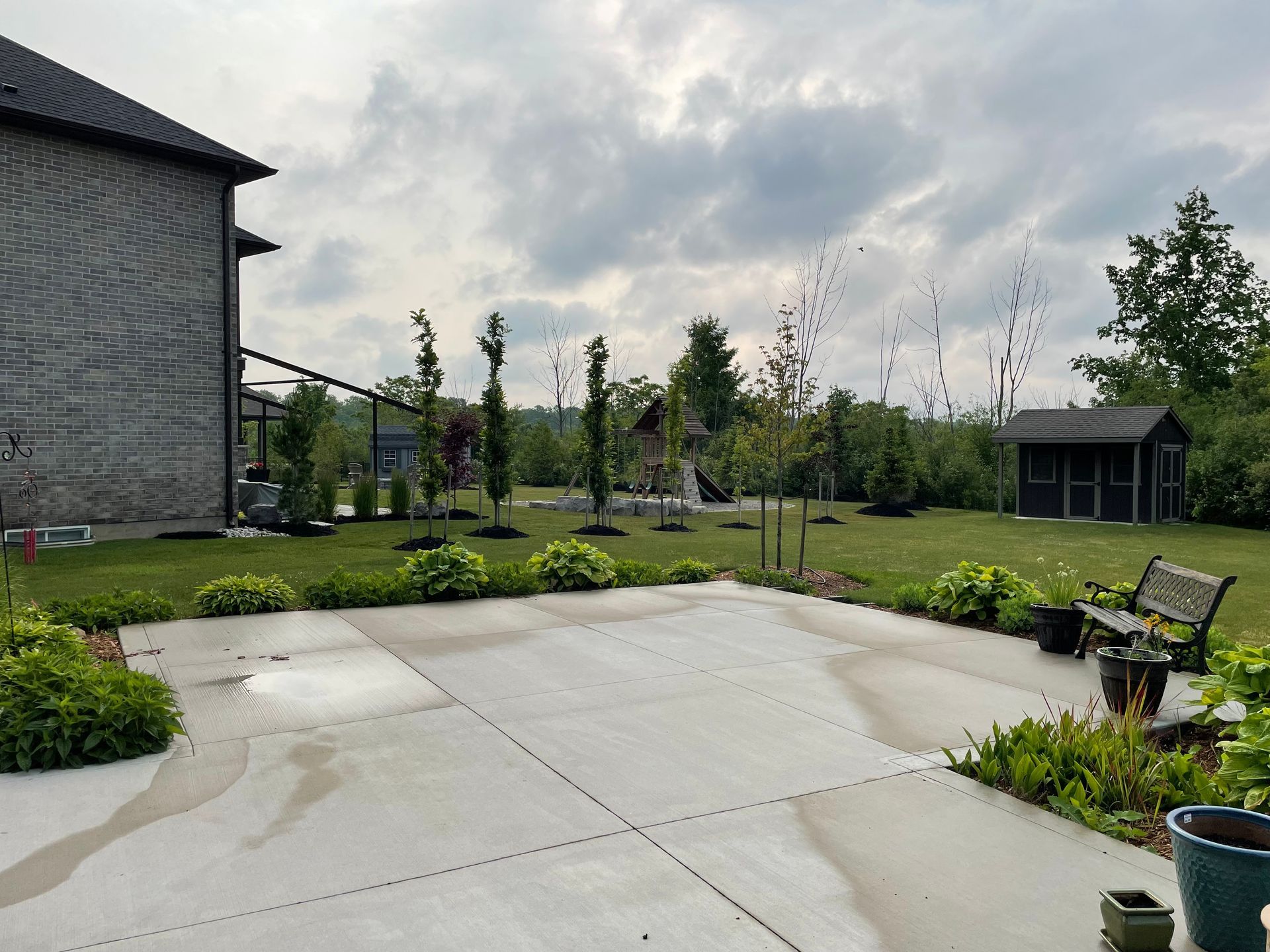 A concrete driveway leading to a house with a shed in the background