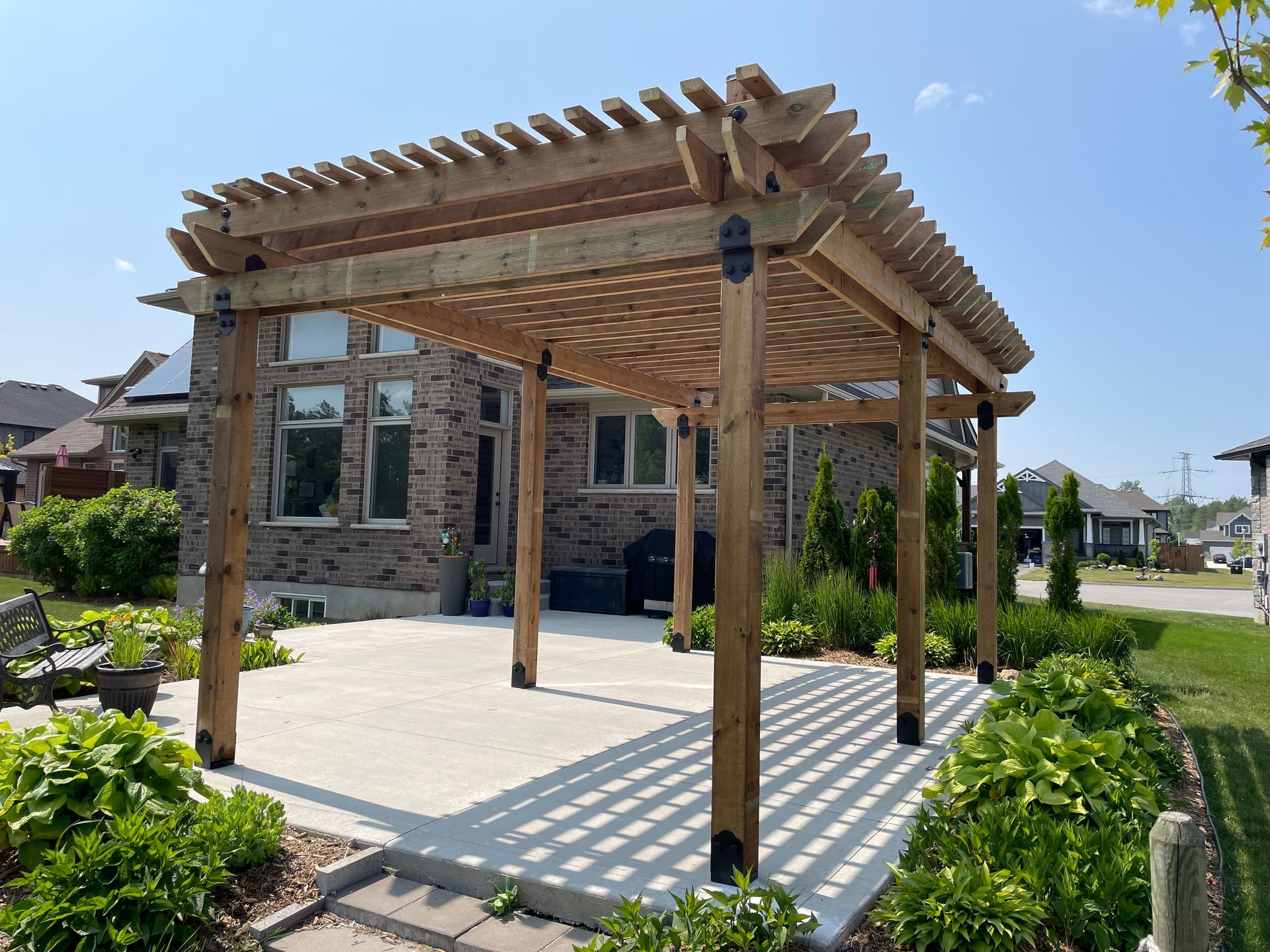 A wooden pergola is sitting in front of a brick house.