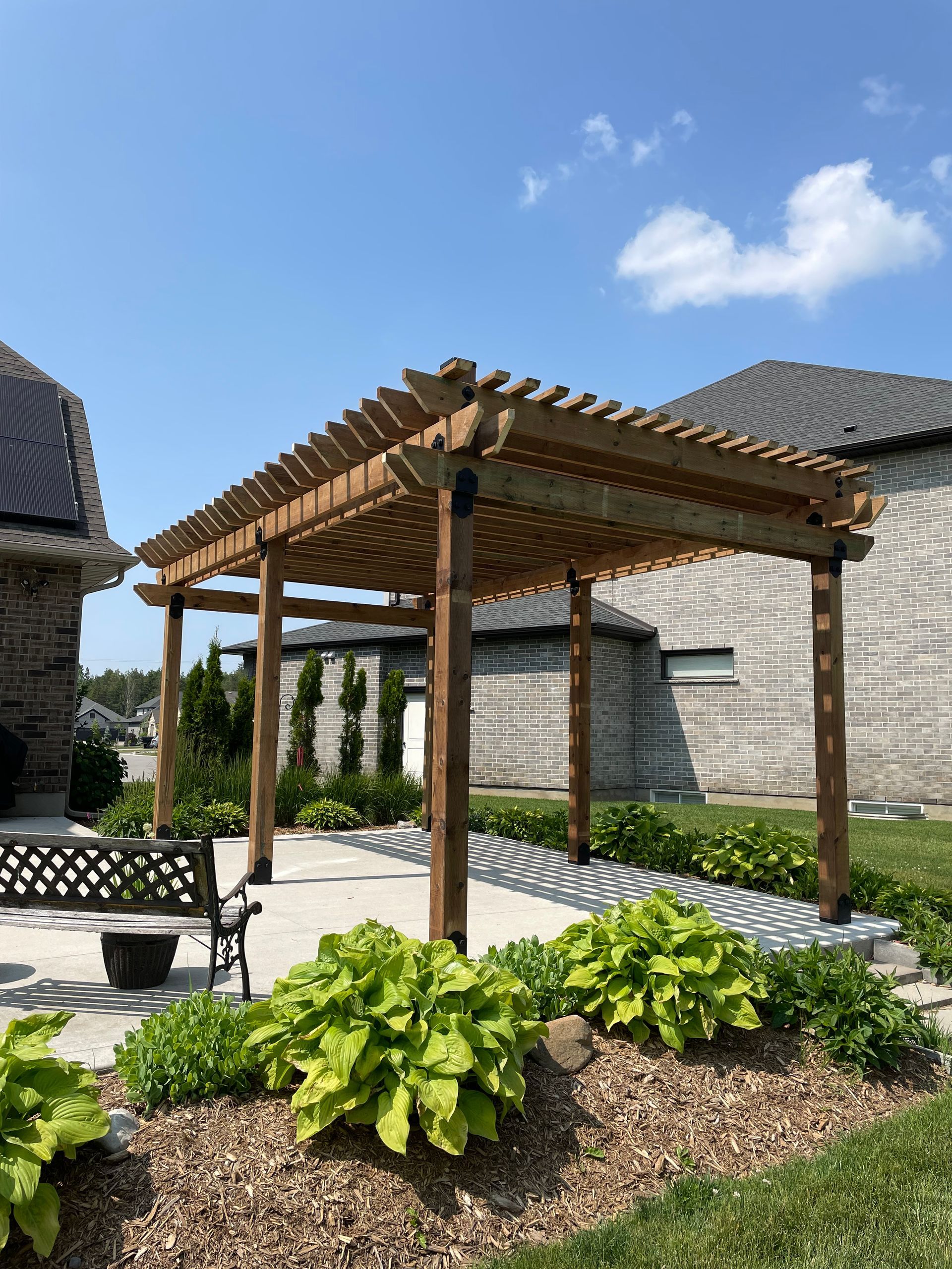 A wooden pergola is in the backyard of a house.