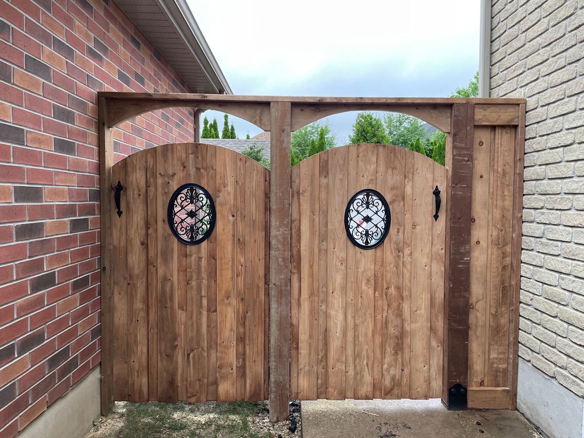A wooden gate with a clock on it is in front of a brick building.
