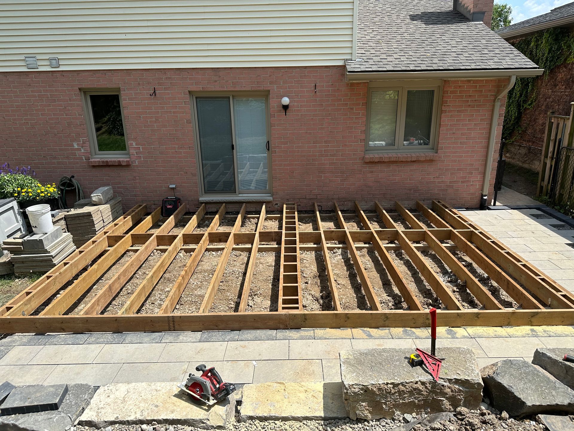 A wooden deck is being built in front of a brick house.