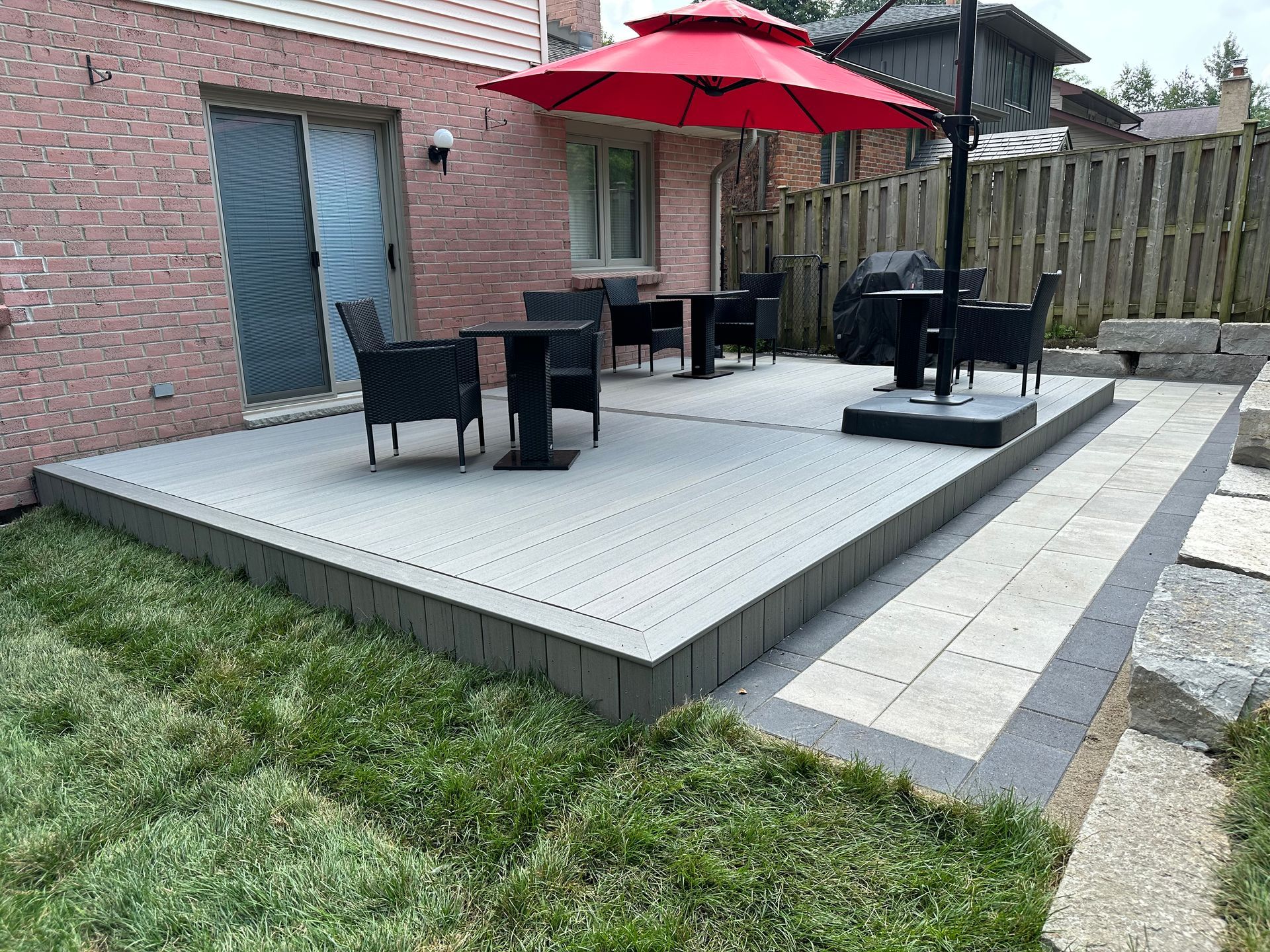A patio with a table and chairs and an umbrella in the backyard of a house.