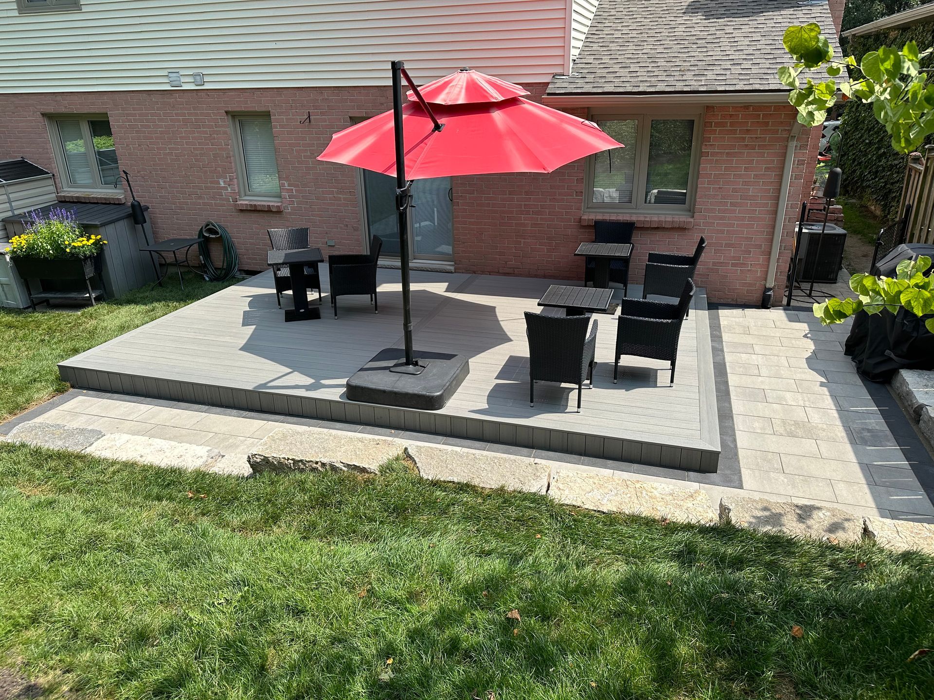 A patio with a red umbrella and chairs in front of a brick house.