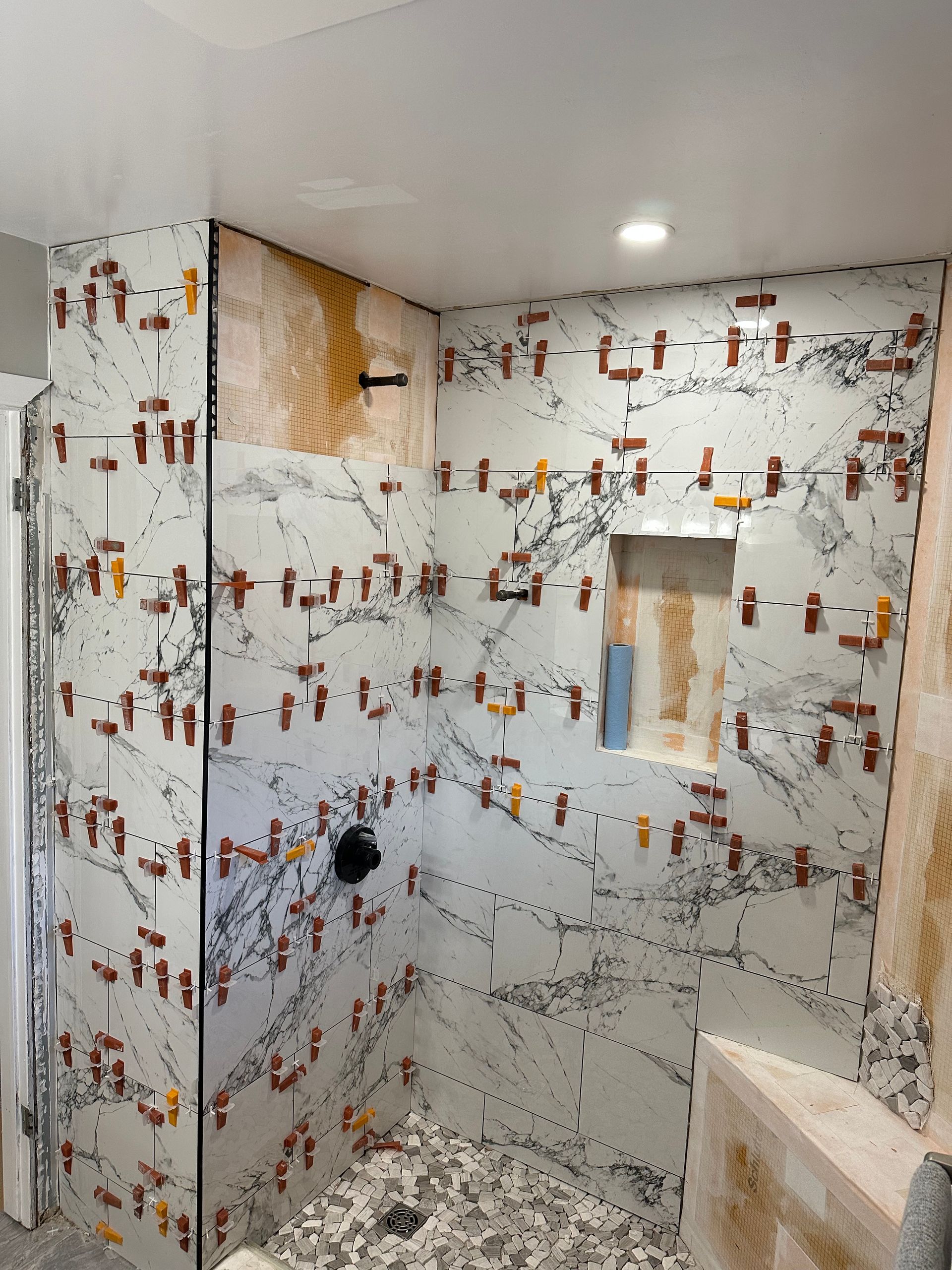 A bathroom with a marble wall and a shower stall being remodeled.