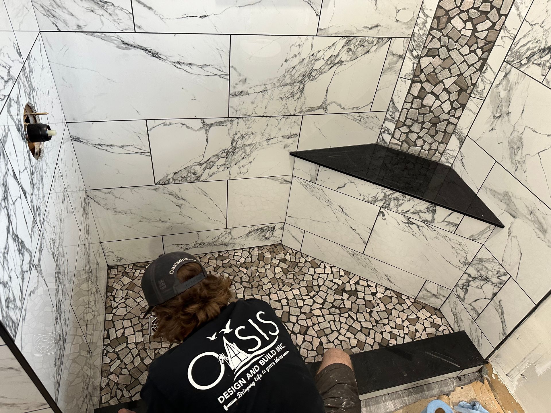 A man wearing a black oasis shirt is working in a shower.