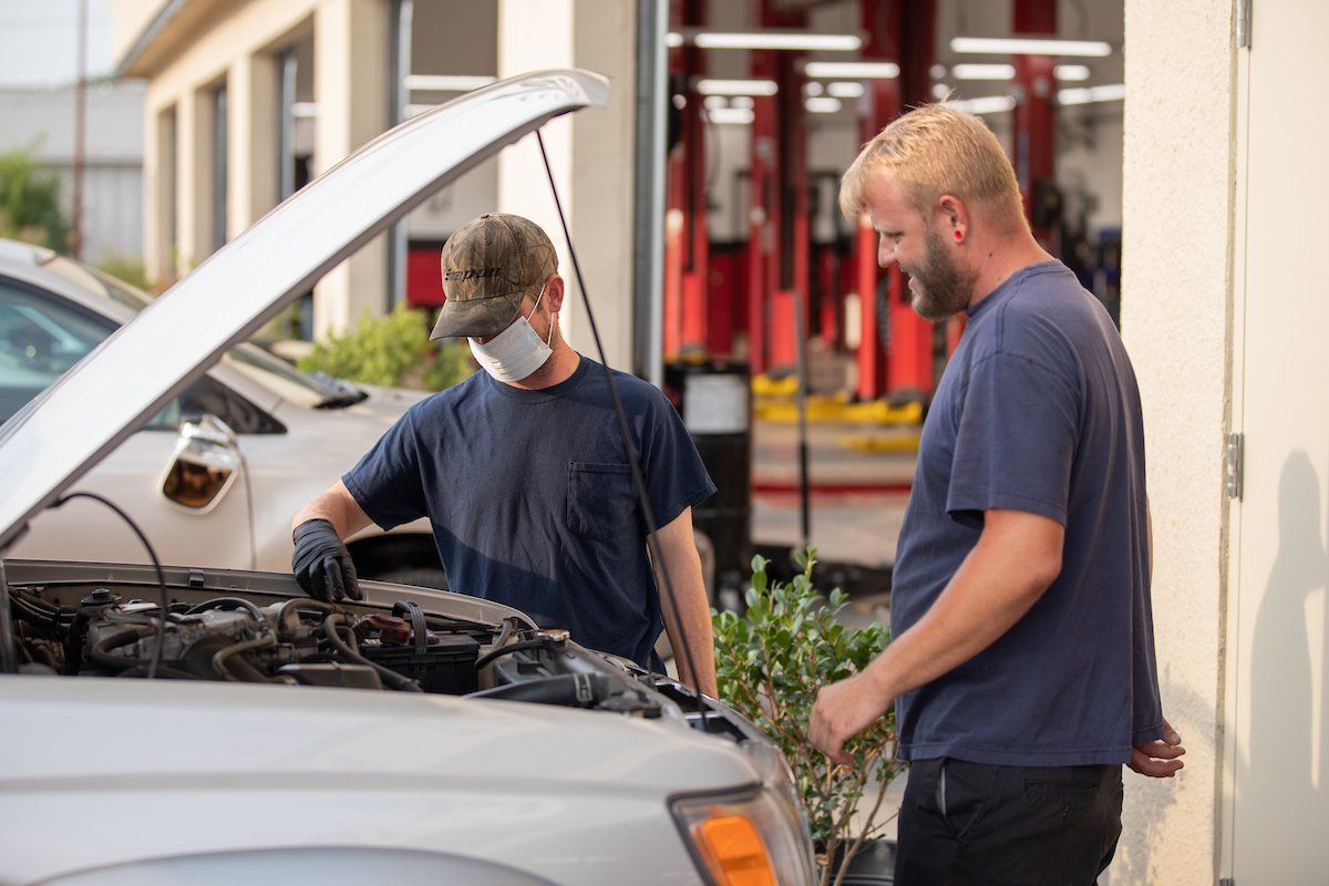 Two men are working on a car with the hood up.