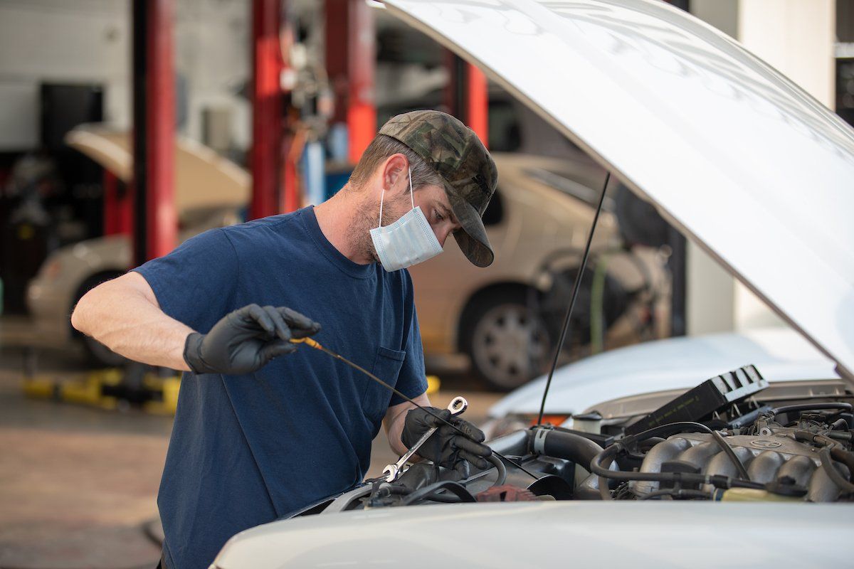 A man wearing a mask is working on a car in a garage.