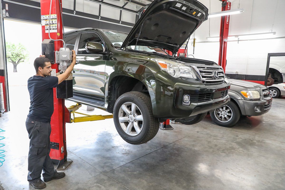 A man is working on a car on a lift in a garage.