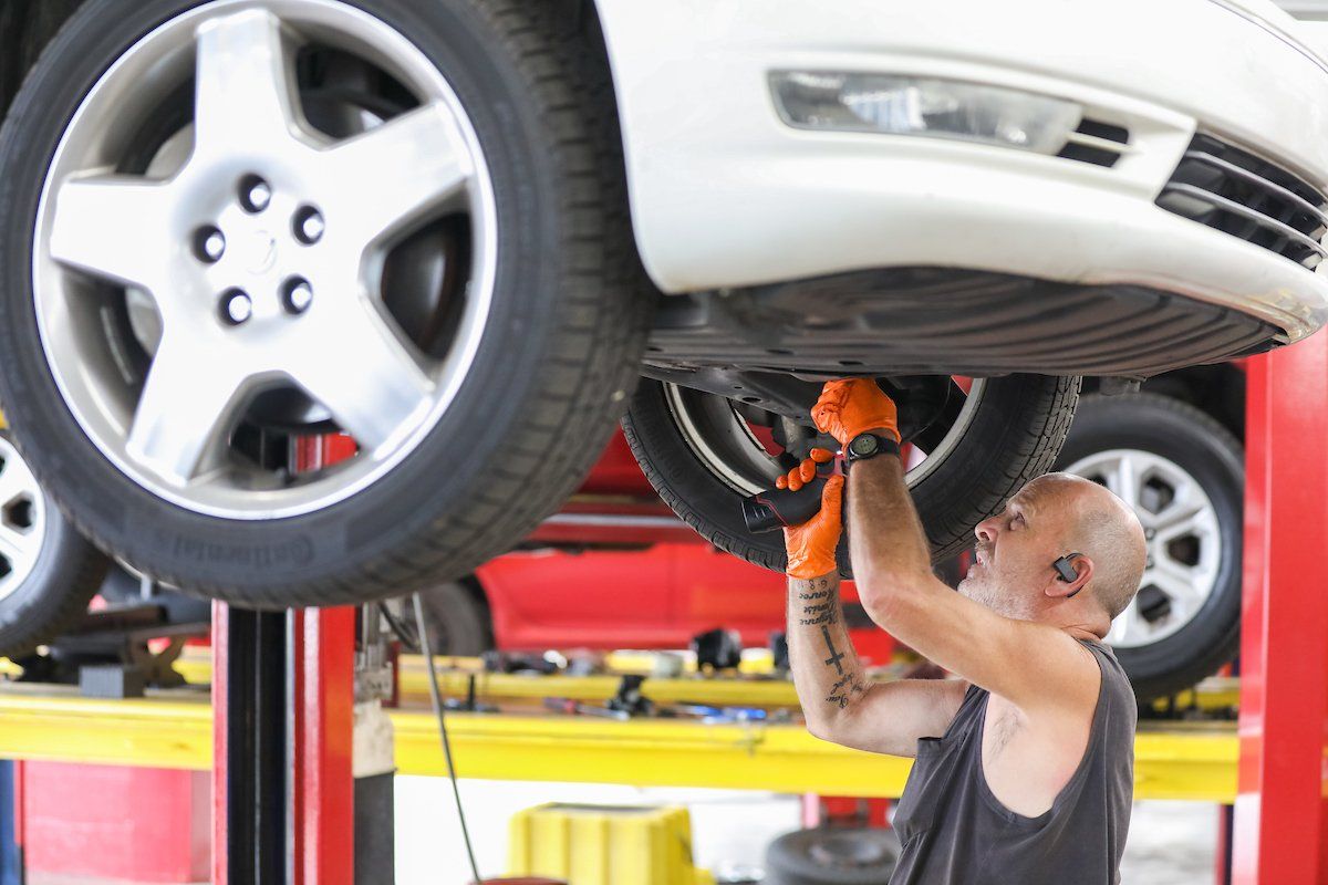 A man is working under a car on a lift in a garage.
