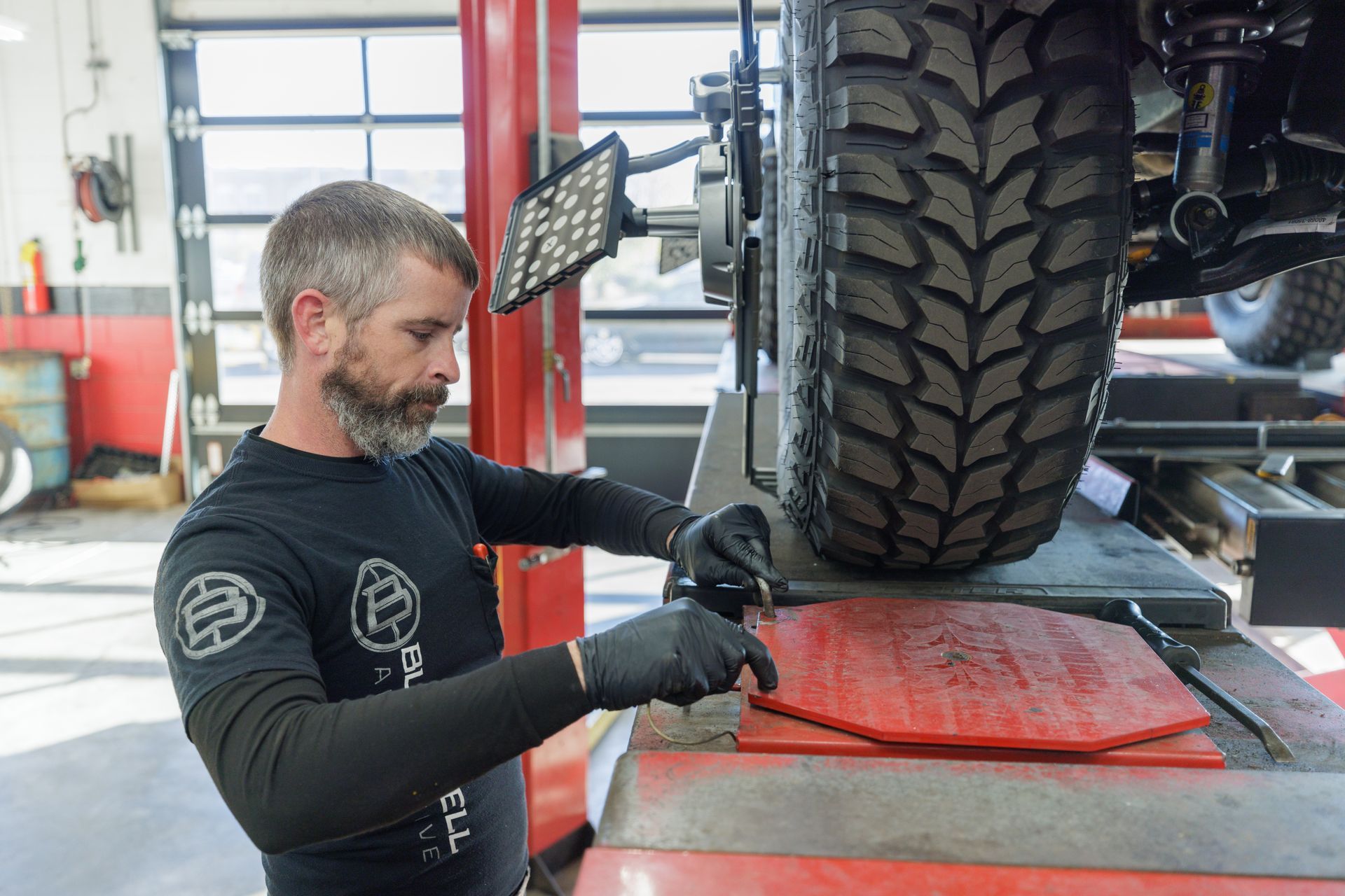Mechanic in black gloves working on car alignment, placing a red plate in a garage.