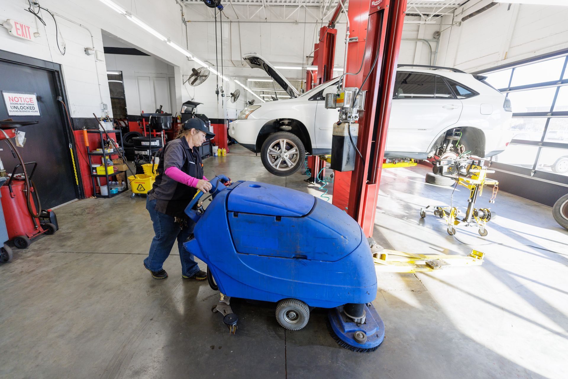 A woman is cleaning the floor of a garage with a machine.
