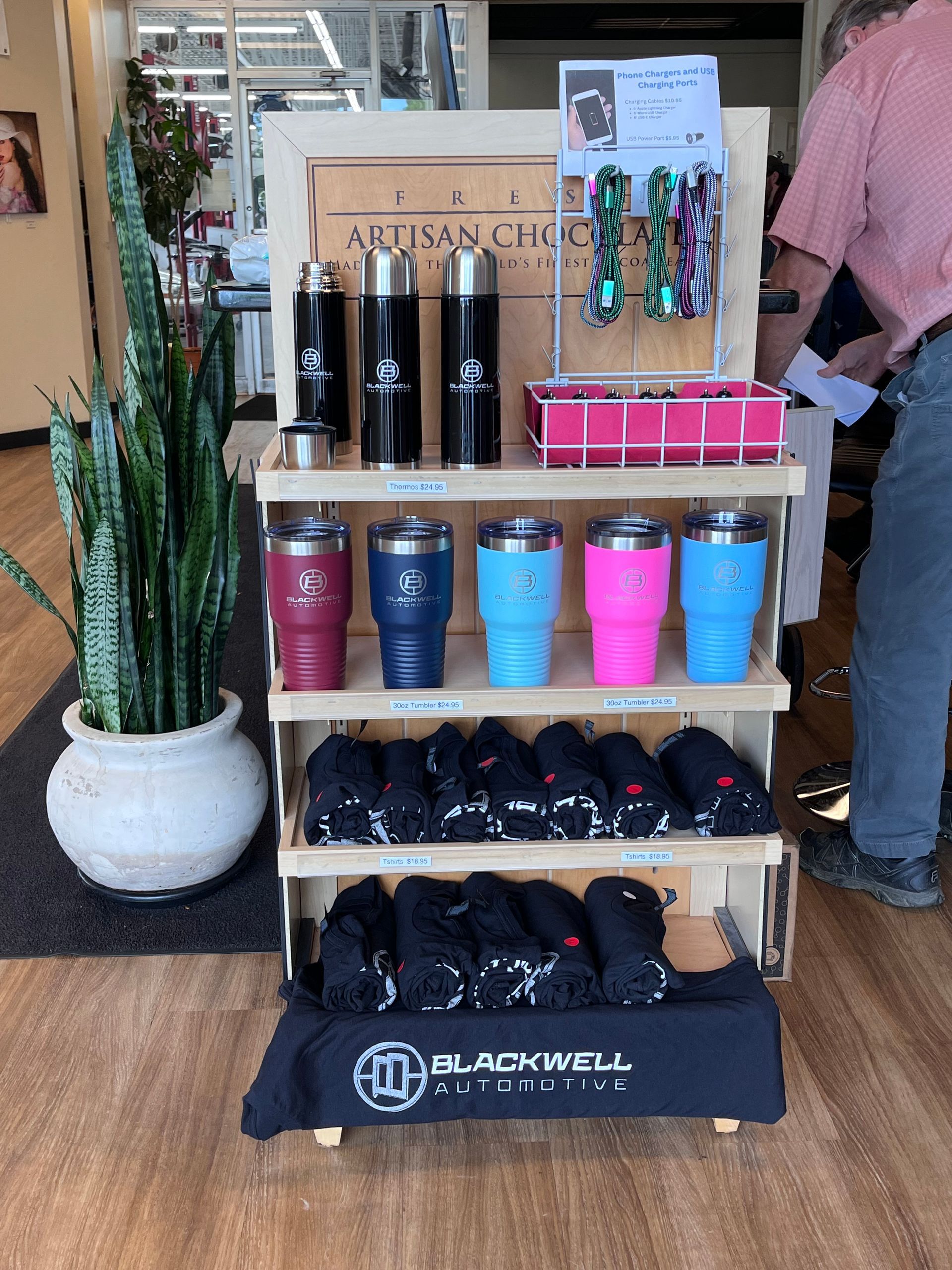 A man is standing in front of a display of tumblers and shirts.