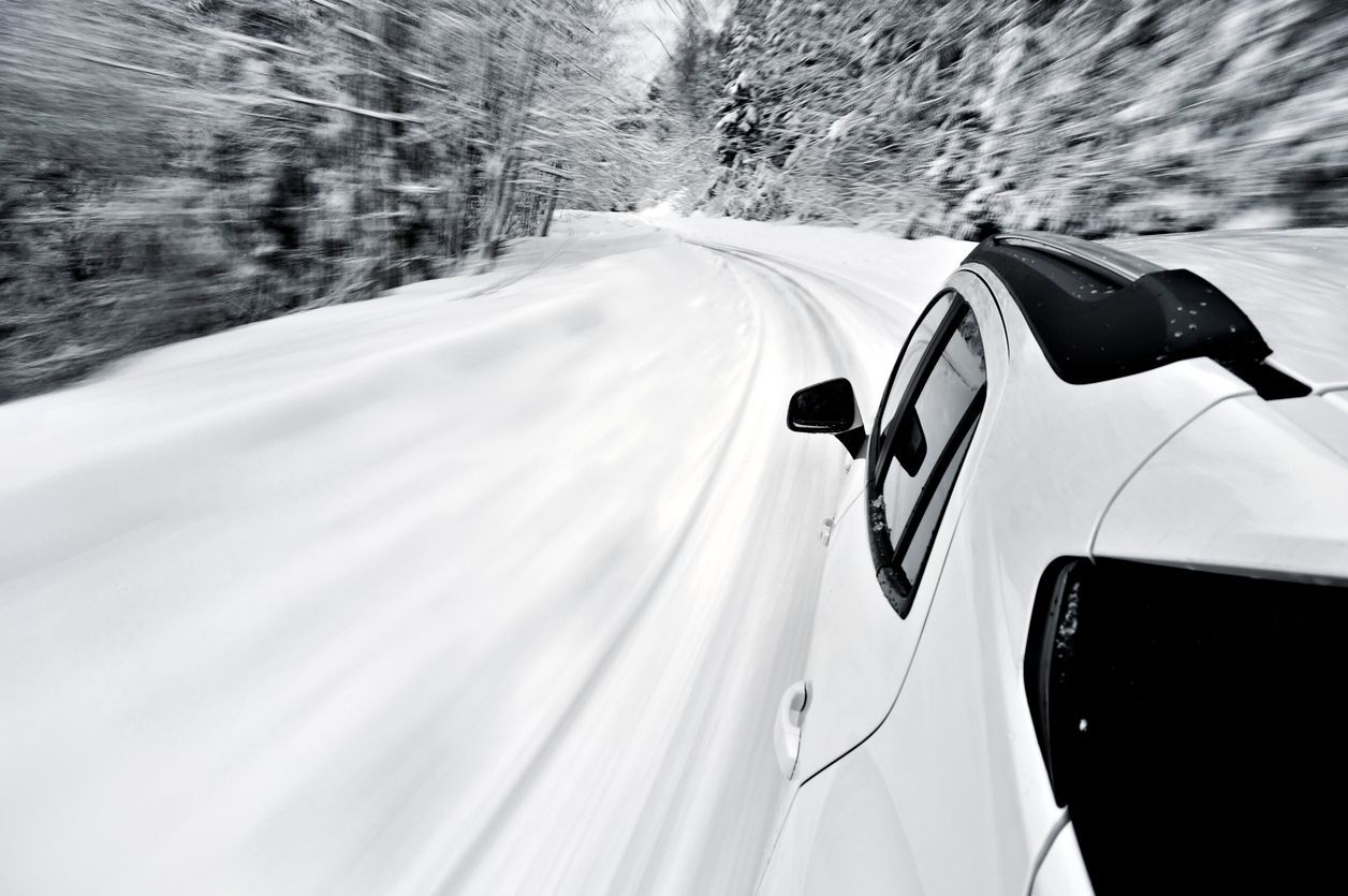 White car driving on a snow-covered road through a forest.