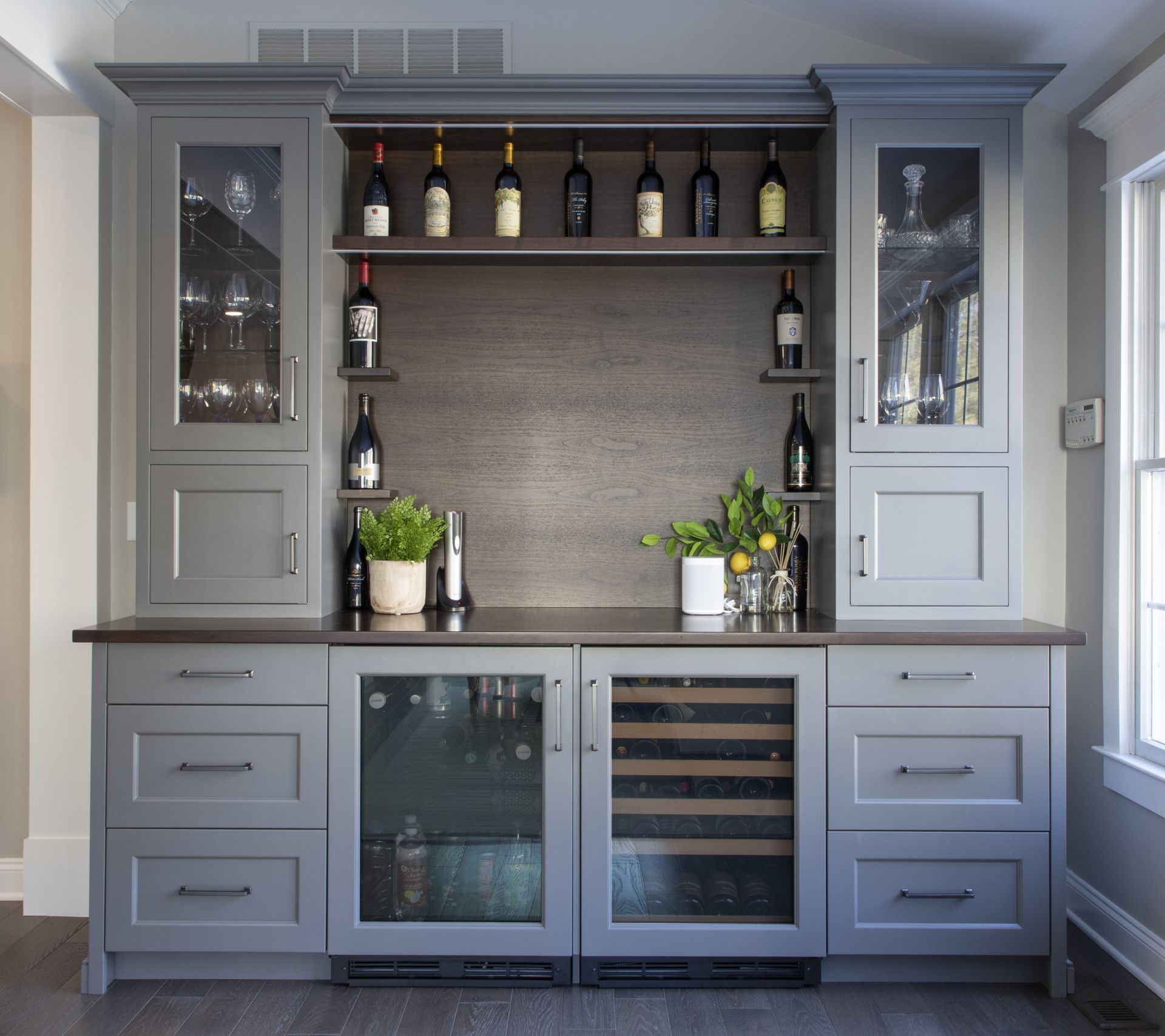 A kitchen with a wine cooler and bottles on shelves