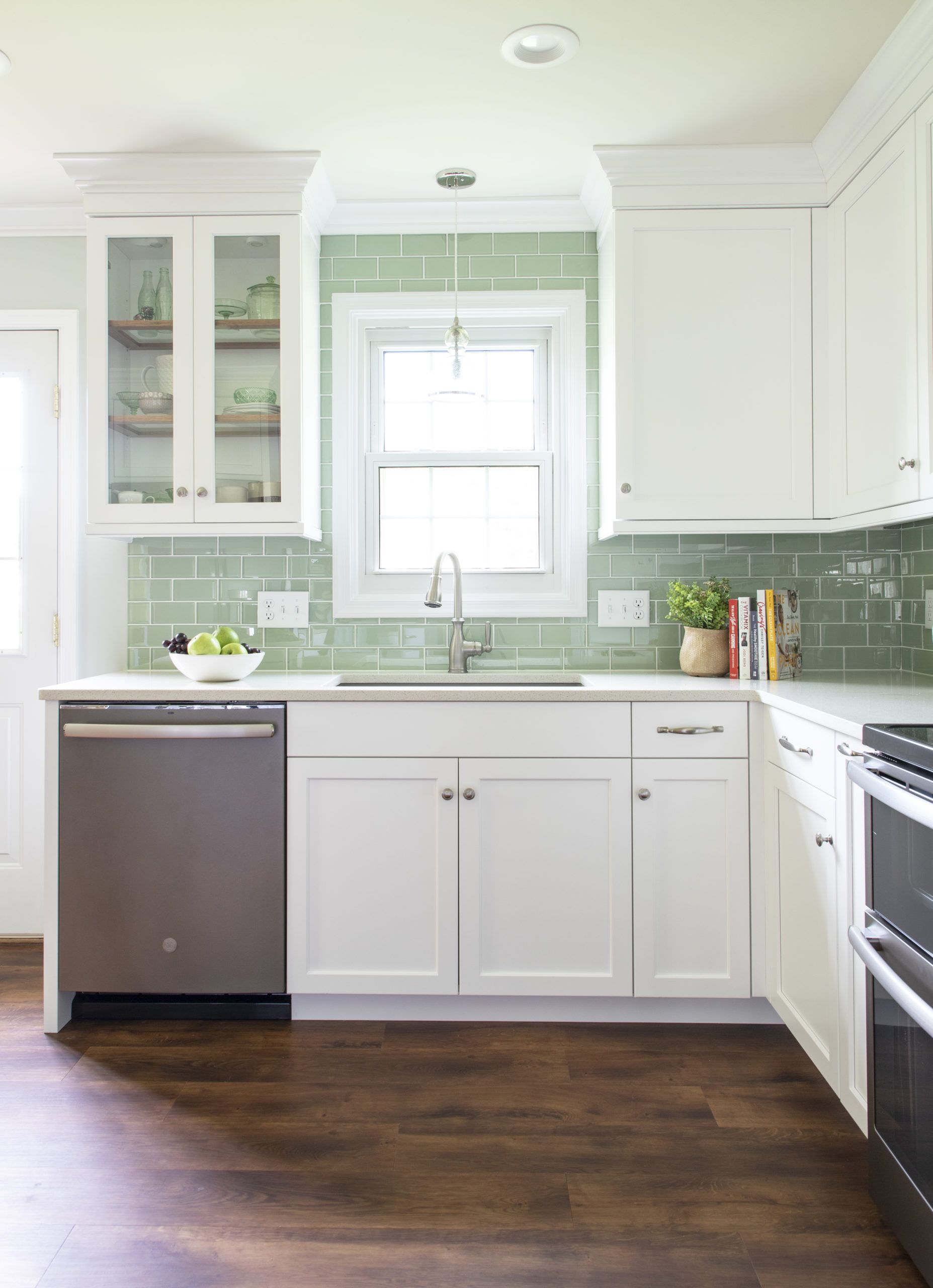 A kitchen with white cabinets , a stainless steel dishwasher , a sink , and a window.