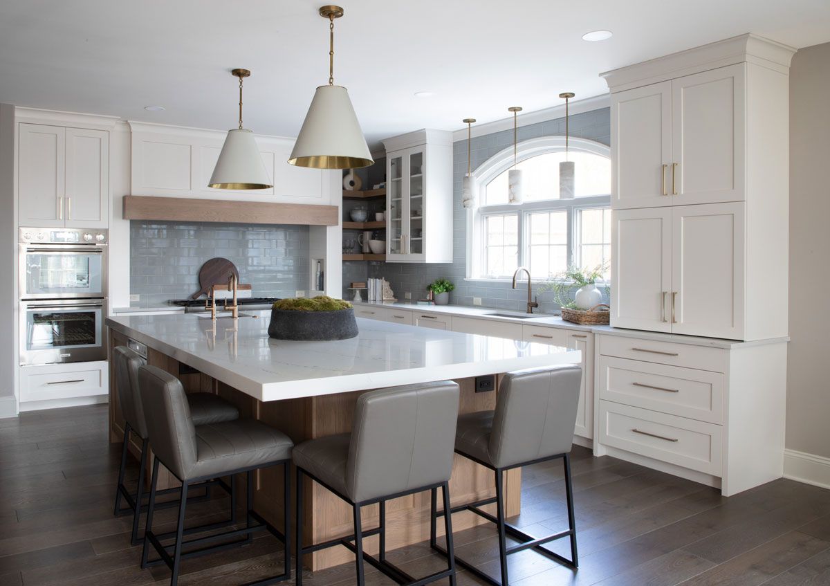 A kitchen with white cabinets , a large island , and stools.