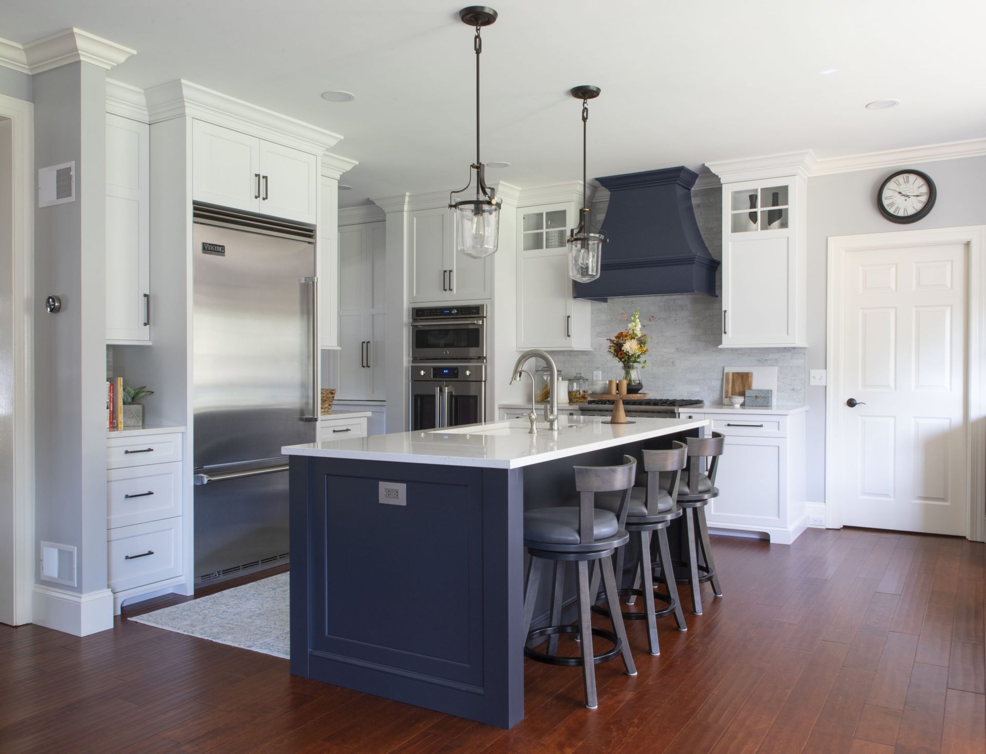 A kitchen with white cabinets , stainless steel appliances , a large island and a clock on the wall.