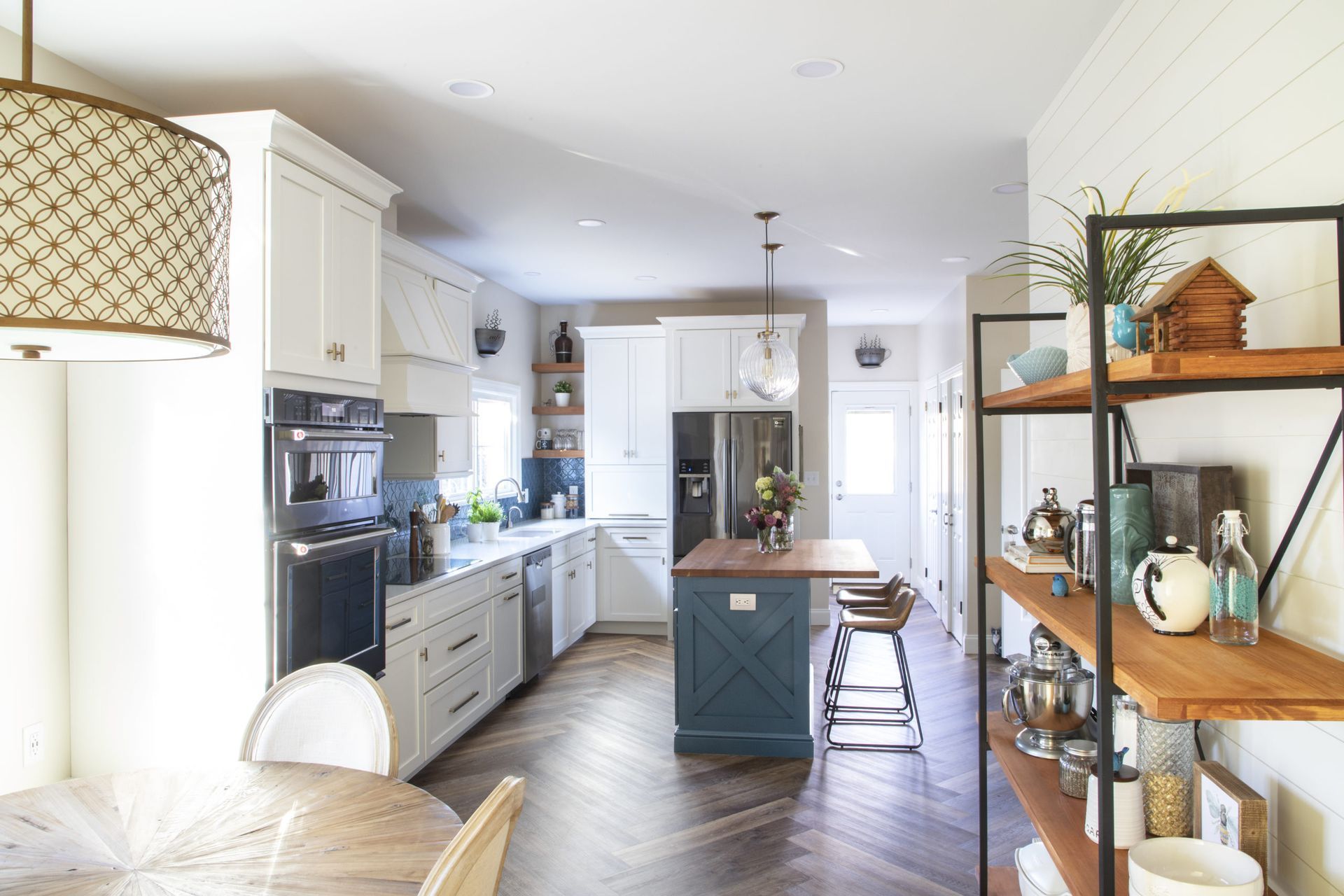 A kitchen with white cabinets , a blue island , a table and chairs.