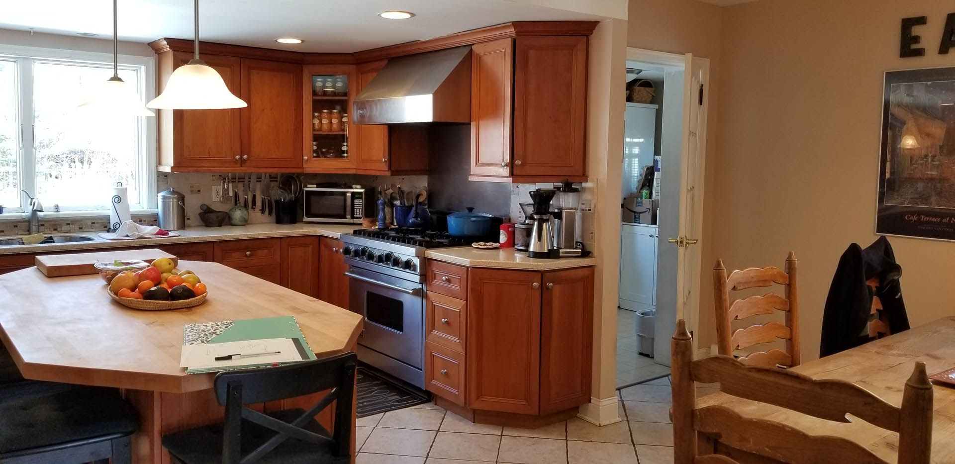 A bright, wood-toned kitchen featuring a large central island, stainless steel appliances, and a dining area to the right.