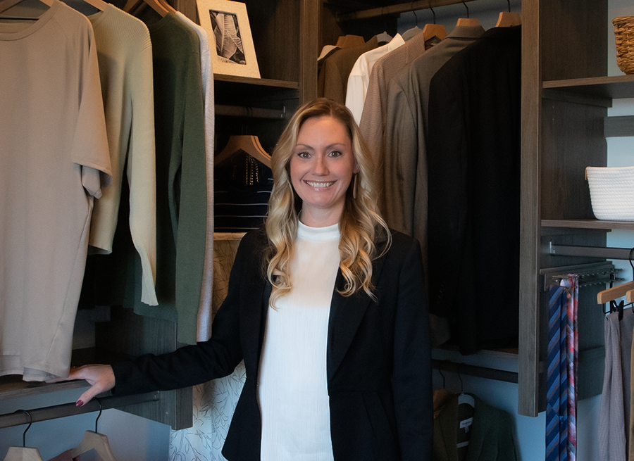 A young man wearing a polo shirt is smiling in a closet.